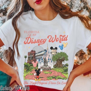 Puede incluir: Camiseta blanca con un gr&aacute;fico colorido de Disney World en Florida. El dise&ntilde;o incluye el texto "FLORIDA Est. 1971 Disney World" y varios puntos de referencia del parque, con Mickey Mouse. Tambi&eacute;n se incluye la frase "The Most Magical Place On Earth".