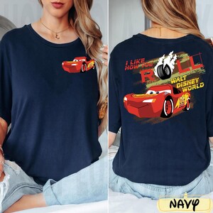 Puede incluir: Camiseta azul marino con un dise&ntilde;o de coche de carreras rojo de dibujos animados en la parte delantera y trasera. La parte trasera de la camiseta tiene el texto "I LIKE HOW YOU ROLL" y "WALT DISNEY WORLD".