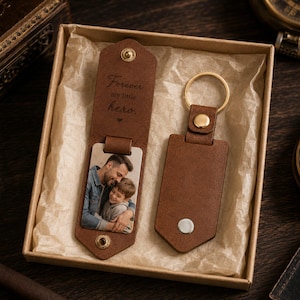 May include: A brown leather keychain and a matching bookmark with a photo and the text "Forever my little hero." The keychain has a gold ring and button. The bookmark has a photo of a man and a child.