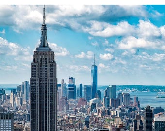 May include: A digital guide for a 3-day weekend itinerary in New York City. The image features the Empire State Building prominently in the foreground, with the city skyline and blue sky with clouds in the background. The text "new york city" is displayed in a bold, dark blue font.