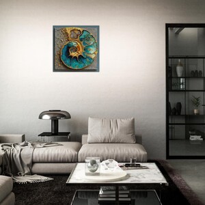 May include: A square wall art piece featuring a detailed, abstract depiction of a nautilus shell. The artwork showcases a spiral design with teal and gold hues, set against a textured gray background. The piece is framed and mounted on a white wall.