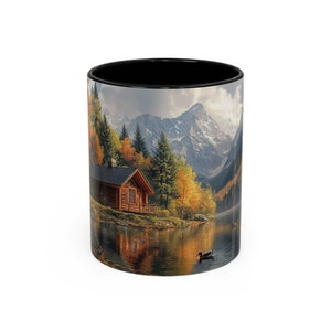 May include: A black coffee mug with a scenic image of a wooden cabin nestled in a mountain valley with a lake in the foreground. The image features a blue sky, snow-capped mountains, and fall foliage.