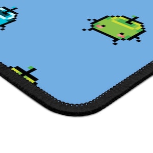 May include: A blue mousepad with a black stitched border. The mousepad features a repeating pattern of pixelated green and blue characters.