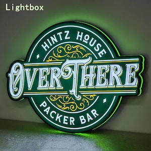 Pode incluir: Um letreiro circular verde iluminado com o texto HINTZ HOUSE OVER THERE PACKER BAR em letras brancas. O design inclui ornamentos decorativos amarelos em forma de volutas e um brilho verde intenso que emana das bordas do letreiro.