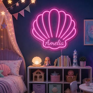 May include: A bright pink neon sign shaped like a seashell with the name Amelia written in cursive script in the centre. The sign is mounted on a dark blue wall above a white shelving unit filled with various toys, books, and decor items.