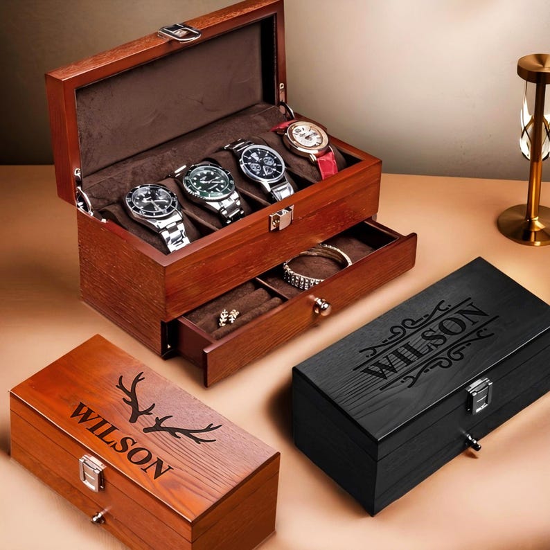 May include: Two wooden watch boxes with a drawer. The top box has a dark brown finish and is open, revealing five watch slots. The bottom box has a light brown finish and is closed. Both boxes have the name "WILSON" engraved on the front.