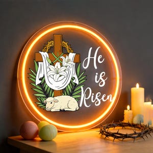 May include: Round illuminated sign with the words "He is Risen" in white script. The sign features a wooden cross, white lilies, a lamb, and a glowing orange border. Decorative candles and a crown of thorns are also visible.
