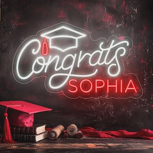 May include: A neon sign with the word "Congrats" and the name "Sophia" in red and white. A graduation cap is above the word "Congrats". A red graduation cap, books, and scrolls are in the foreground.