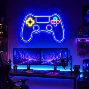May include: A wall-mounted neon sign shaped like a video game controller with a bright blue outline. The controller features a glowing yellow directional pad on the left and four circular buttons in green, pink, and red on the right side.