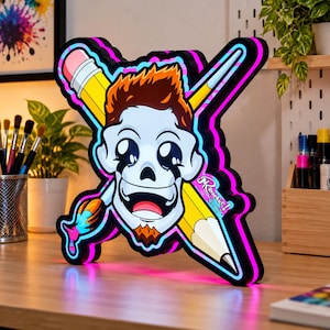 Pode incluir: Um letreiro LED personalizado com uma caveira de desenho animado com cabelo castanho e cavanhaque, posicionada &agrave; frente de um l&aacute;pis amarelo e um pincel cruzados. A borda preta tem luzes de estilo n&eacute;on em rosa e azul.