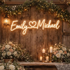 Può includere: Una scena di matrimonio accogliente con un'insegna al neon che recita "Emily & Michael" in corsivo, con un simbolo a forma di cuore. L'insegna è montata su uno sfondo di legno rustico, completata da composizioni floreali e candele.