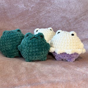 May include: Three crocheted frog plushies. One is green, one is white, and one is white with a purple underside.