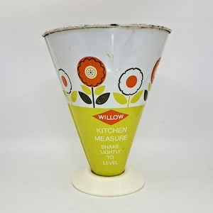May include: A vintage Willow kitchen measure with a white base. The cone-shaped measure is white at the top with orange and white flower designs. The bottom half is yellow with the text "WILLOW KITCHEN MEASURE SHAKE LIGHTLY TO LEVEL."