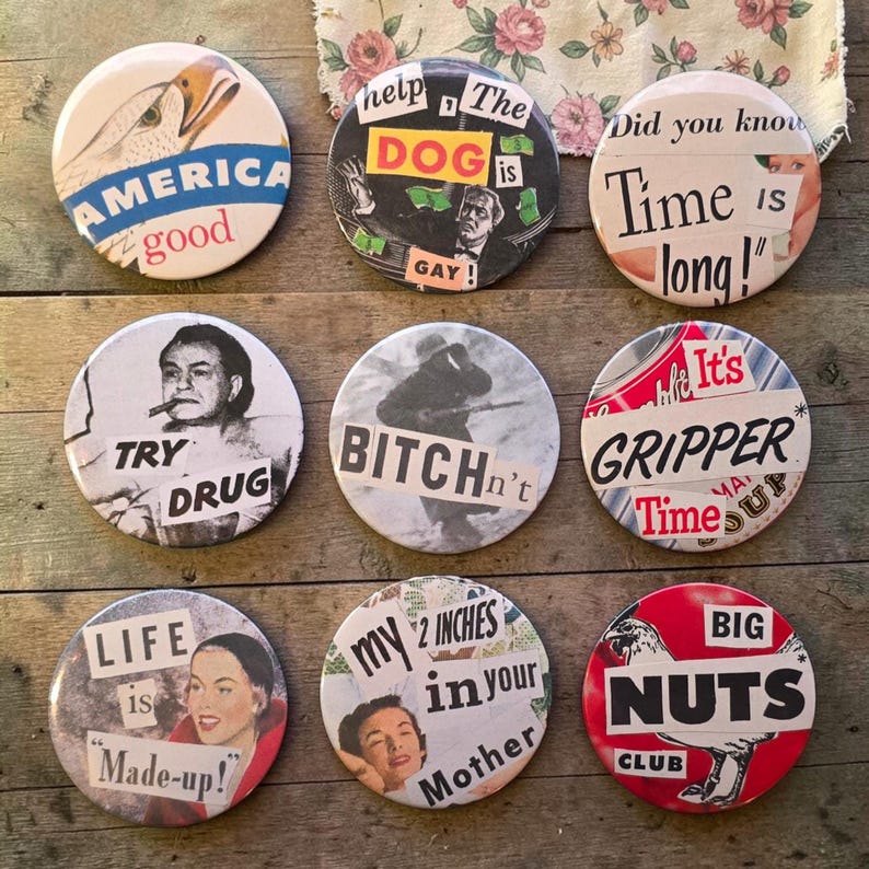 Puede incluir: Una colecci&oacute;n de nueve botones vintage con diversos dise&ntilde;os y textos. Los botones presentan im&aacute;genes de un &aacute;guila, una mujer y otros gr&aacute;ficos, junto con frases como "America good", "Big Nuts Club" y "Time is long!" sobre una superficie de madera.