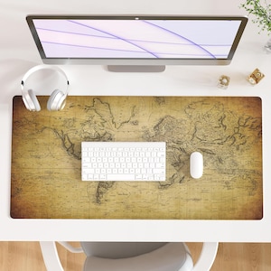 May include: A computer desk setup featuring a large monitor, white keyboard, and mouse. A world map design mousepad in shades of brown and tan covers the desk. White headphones rest on the mousepad. A small bear figurine and a decorative cube are also on the desk.