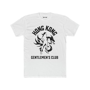 May include: White t-shirt with a black graphic design. The graphic features a woman standing in front of a dragon with the text "Hong Kong Gentlemen's Club".