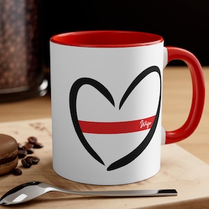 May include: White ceramic mug with a red rim and handle. The mug features a black outline of a heart with a red stripe across the middle and the word "Wife" written in black inside the heart.
