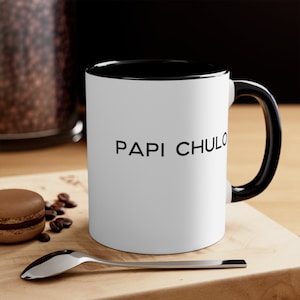 May include: White ceramic mug with a black rim and handle. The mug has the text "PAPI CHULO" printed in black on the front.