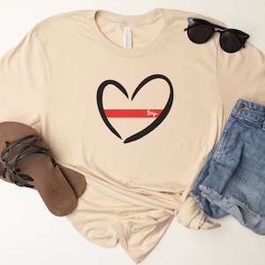 May include: A beige t-shirt with a black outline of a heart with a red line through the middle. The text "Wife" is written inside the heart.