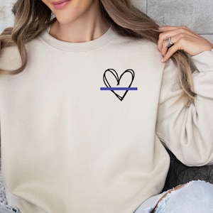 May include: A beige sweatshirt with a black hand-drawn heart and a thin blue line across the center.