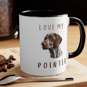 Puede incluir: Taza de cerámica blanca con borde y asa negros. La taza tiene una ilustración marrón y blanca de un perro Braco Alemán de Pelo Corto y el texto "LOVE MY POINTER".