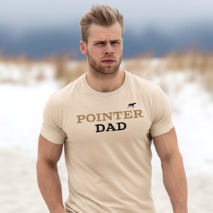 May include: A beige t-shirt with black text that reads "POINTER DAD" and a small black silhouette of a dog above the text.