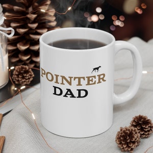 May include: White ceramic coffee mug with a brown silhouette of a dog and the text "POINTER DAD" in brown and black lettering.