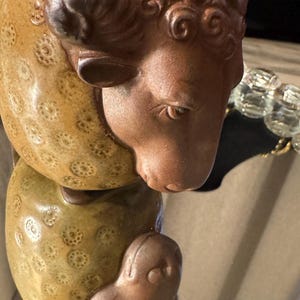 May include: A ceramic sheep-shaped planter with a brown head and a tan body. The sheep's head is detailed with curly wool and a focused expression. The body has a textured, dotted pattern.