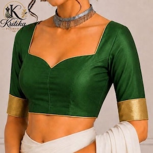 May include: A dark green blouse featuring a sweetheart neckline with gold piping trim, short sleeves with wide gold cuffs, and a structured bodice. The garment is paired with a white fabric draped at the waist and a silver fringe choker necklace.