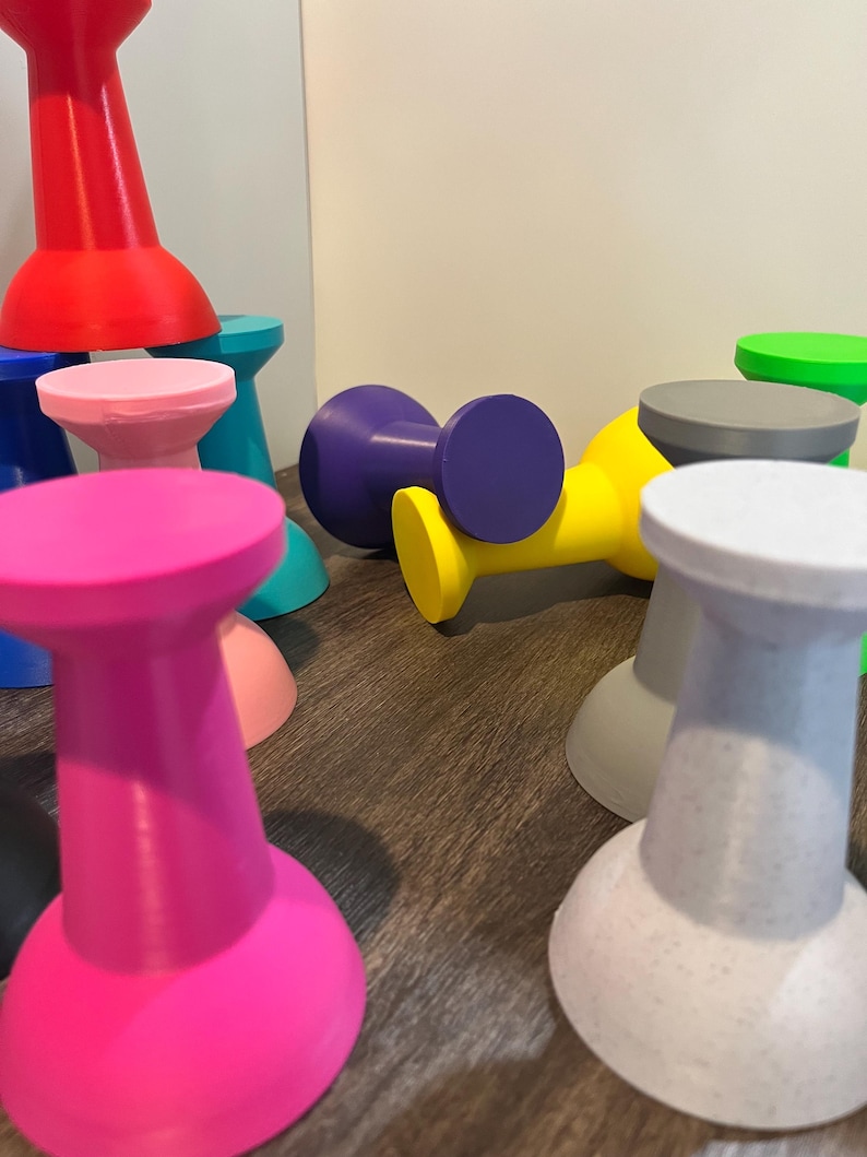Pu&ograve; includere: Una collezione di piccoli oggetti a forma di rocchetto in vari colori solidi, tra cui rosa acceso, rosso, blu, giallo, viola, rosa chiaro, grigio e verde. Ogni oggetto presenta un'ampia base circolare e una parte superiore abbinata collegate da un collo stretto.
