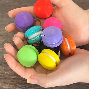 Könnte beinhalten: Ein Set aus bunten Schlüsselanhängern in Macaron-Form, darunter lila, rot, grün, gelb und blau. Die Schlüsselanhänger sind aus Kunststoff und haben eine glatte, glänzende Oberfläche.