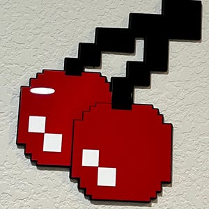 May include: A pixelated cherry with a black stem, in a retro video game style. The cherry is red with white pixels, and the stem is black.