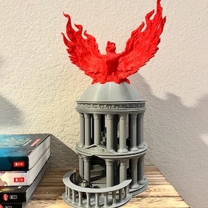 May include: A 3D printed gray temple with a red phoenix on top. The temple has columns and a balcony. A black and gold dice is on the balcony.