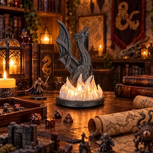 May include: A black dragon figurine perched atop a glowing white base that mimics the appearance of flickering flames. The dragon has detailed scales and wings, and the base emits a warm light, creating a dramatic effect on the table.