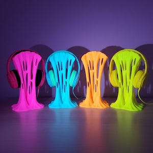 以下が含まれることがあります： ピンク、青、オレンジ、黄色の4色のヘッドフォンスタンド。それぞれがヘッドフォンを1つずつ保持しています。スタンドはユニークな溶けたようなデザインです。背景は紫色のグラデーションで、スタンドは木製の表面にあります。