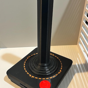 May include: A black vintage-style joystick with a red button and an orange dashed circle around the base.