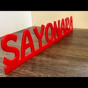 Può includere: Un cartello rosso stampato in 3D che recita "SAYONARA".