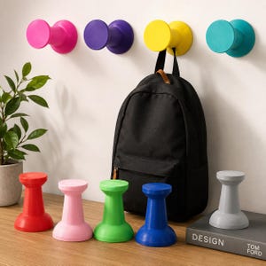 Pu&ograve; includere: Una collezione di ganci da parete colorati e supporti indipendenti a forma di rocchetto in rosa, viola, giallo, turchese, rosso, rosa chiaro, verde, blu e grigio. Uno zaino nero &egrave; appeso al gancio da parete giallo sulla parete bianca.
