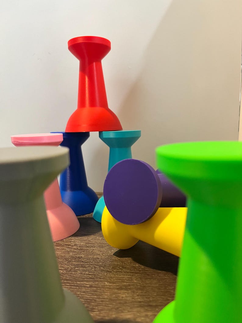 collection of colorful, abstract, giant pushpin-shaped objects in various colors, including red, blue, green, yellow, purple, and pink. The objects are arranged in a playful, stacked composition, with some lying on their sides.