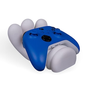 May include: A blue Xbox controller resting in a white hand-shaped stand. The stand has three fingers and a thumb.
