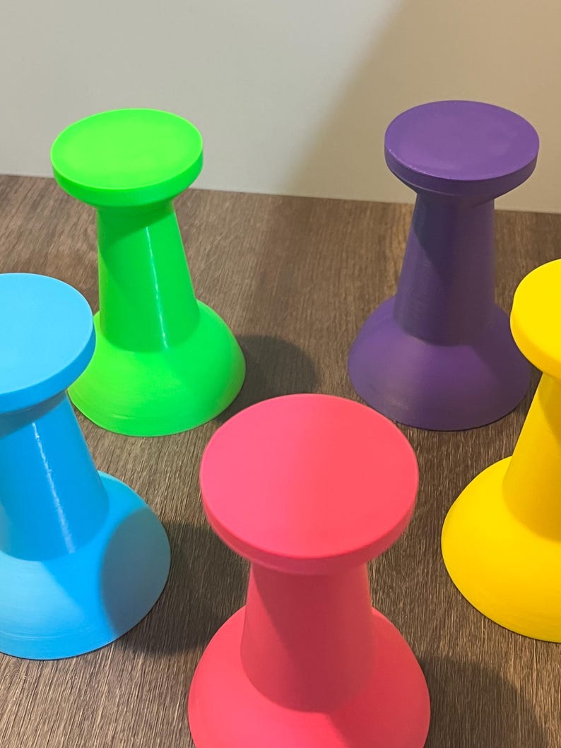 Pu&ograve; includere: Un set di cinque piccoli sgabelli monocolore con base svasata e piano circolare. Gli sgabelli sono colorati in verde neon brillante, viola vibrante, azzurro cielo, rosa acceso e giallo sole, ognuno con una finitura opaca e liscia.