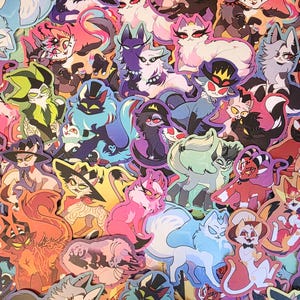 May include: A collection of colorful stickers featuring cartoon cats with different expressions and poses. The stickers are on a white background and feature various colors, including pink, blue, green, red, and black.