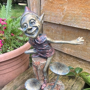 May include: A whimsical garden statue of a smiling elf with a pointed hat, standing on a tree stump with three mushroom-shaped stools. The elf is painted in shades of gold, brown, and red.