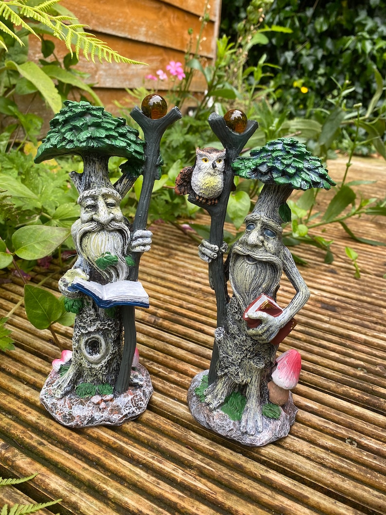 Pu&ograve; includere: Due fantasiose statuette a forma di albero con volti dettagliati, lunghe barbe e chiome frondose. Una tiene un libro, l'altra un bastone con un gufo e un globo di vetro. Le statuette sono dipinte in tonalit&agrave; di verde, marrone e grigio, con accenti di funghi.