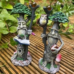 Pu&ograve; includere: Due statue da giardino fantasiose raffiguranti figure simili ad alberi con lunghe barbe e che tengono bastoni. Una figura tiene in mano un libro, l'altra ha un gufo appollaiato sul suo bastone. Le statue hanno cime verdi a forma di albero e sono su una superficie di legno.