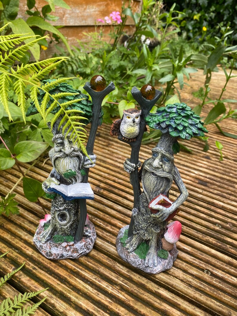 Pu&ograve; includere: Due statue da giardino fantasiose di figure simili ad alberi con lunghe barbe e che tengono bastoni sormontati da globi color ambra. Una figura tiene un libro, l'altra ha un gufo. Le statue sono su un ponte di legno.