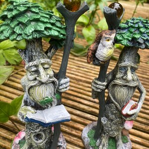 Pu&ograve; includere: Due fantasiose statuette a forma di albero con volti dettagliati, barbe e cime frondose. Una tiene un libro aperto, l'altra un piccolo libro. Entrambe hanno un bastone sormontato da un globo marrone. Un gufo &egrave; appollaiato su un bastone. Le statuette sono su una superficie di legno.