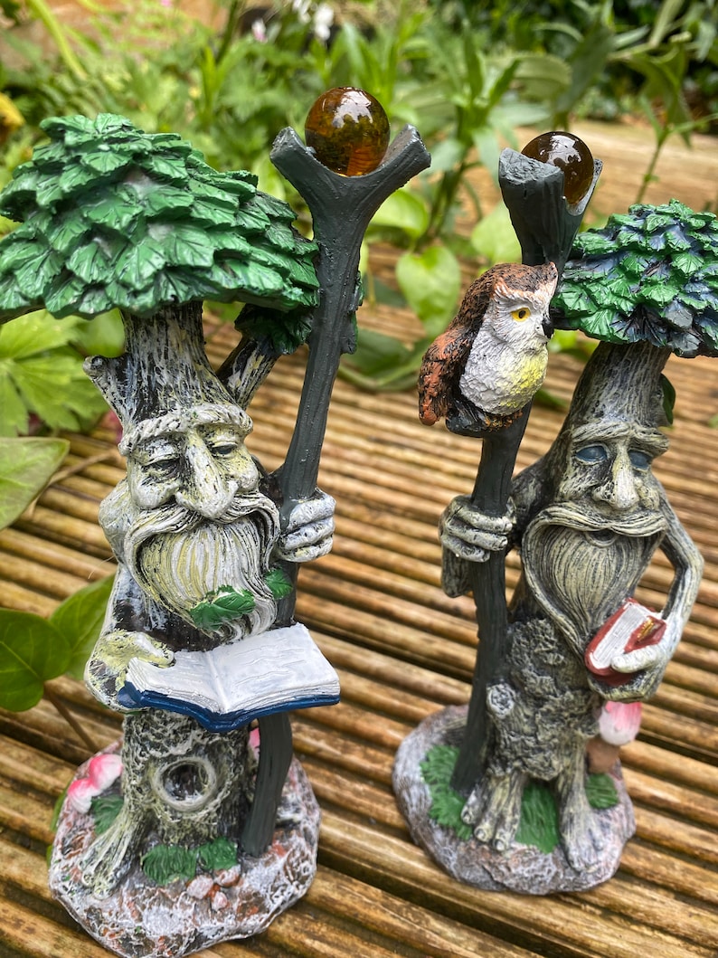 Pu&ograve; includere: Due fantasiose statuette a forma di albero con volti dettagliati, barbe e cime frondose. Una tiene un libro aperto, l'altra un piccolo libro. Entrambe hanno un bastone sormontato da un globo marrone. Un gufo &egrave; appollaiato su un bastone. Le statuette sono su una superficie di legno.
