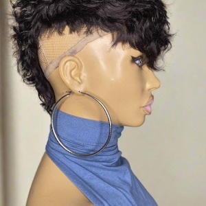 May include: A mannequin head displaying a short, dark, curly wig with a modern, textured style. The wig has a lace front. The mannequin is wearing a blue top and large silver hoop earrings.