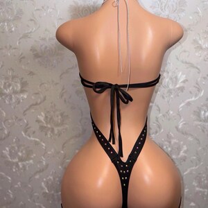 May include: Black lingerie set with rhinestone detailing. The set features a halterneck top and high-leg bottoms with thigh straps. The lingerie is shown on a mannequin.
